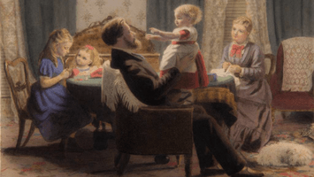 A family sits around a table. A child sits in her father's lap, arms outstretched.