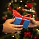 A closeup of a wrapped present being given with a christmas tree in the background.