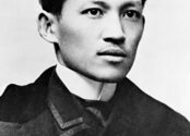 Black and white photograph of a young man, cleanly shaven, with a small swoop of dark hair across his forehead. He is wearing a white collar and a nice, black coat. 