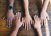 Five hands placed on a wooden background.