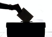 A silhouette of a hand placing a piece of paper into a box.