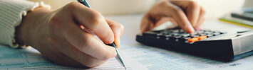 A person fills out the 1040 tax form, with the help of a calculator