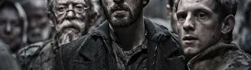 Chris Evans is center screen, dressed in dark, ripped clothing, surrounded by co-stars Jamie Bell and John Hurt in a still frame from the movie Snowpiercer.