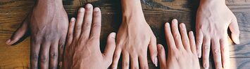 Five hands placed on a wooden background.