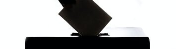 A silhouette of a hand placing a piece of paper into a box.