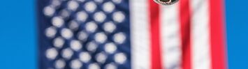 A surveillance camera in the foreground, in front of a blurred out American flag in the background.