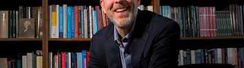 Mark David Hall looks into the camera, sitting in front of a bookcase.